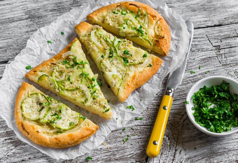 pizza with zucchini, onion, cheese and sesame seeds on a light wooden background