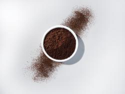 Overhead view of a white bowl filled to the top with a dark brown powder. To either side, powder is scattered diagonally away from the bowl. 