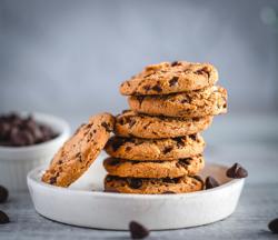A stack of chocolate chip cookies on white plate and scattered chips