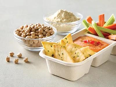 Whole chickpeas & chickpea flour next to chickpea crisps, hummus, carrots & celery