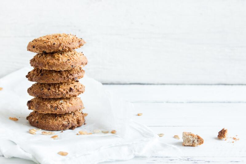 Image of a stack of cookies with oats scattered around on a white background.