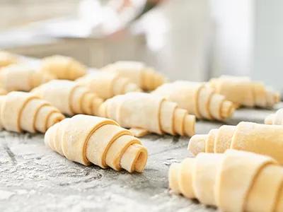 Uncooked croissants dough rolled up on a floured surface. 
