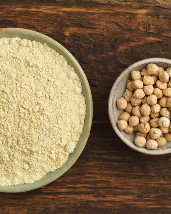 Chickpea flour and intact chickpeas in bowls on brown table